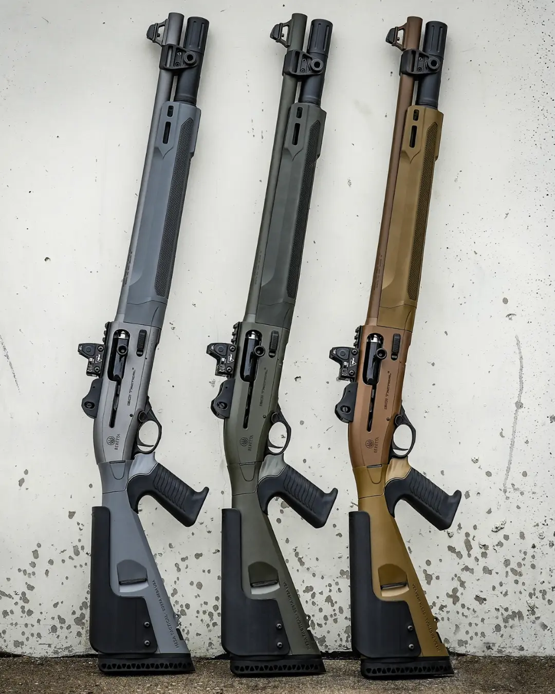 Three matching tactical shotguns in different colors leaned against a concrete wall