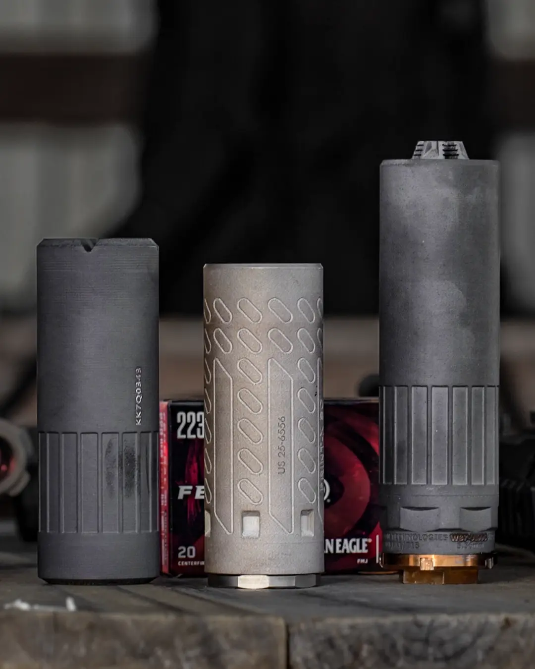Three 3D printed suppressors in front of ammunition boxes on a shooting range table